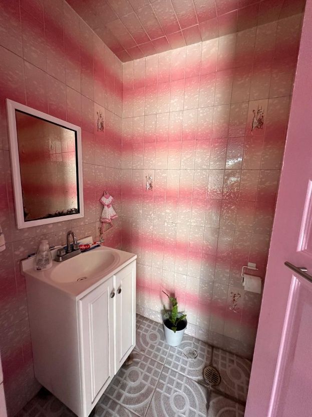 Baño con azulejo en tonos rosas, lavabo con gabinete y espejo