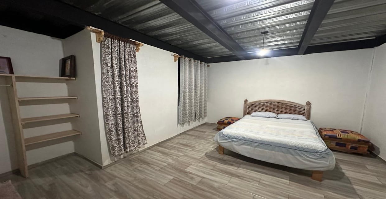 Habitación amueblada con cama matrimonial, cortinas y repisas de madera