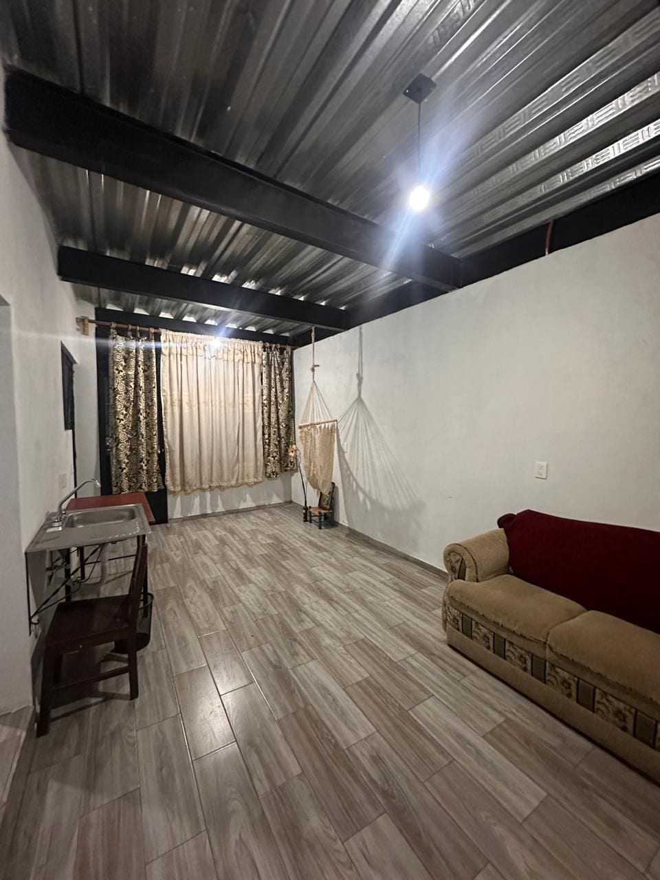 Estancia con piso laminado tipo madera y ventana con cortinas, mostrada amueblada