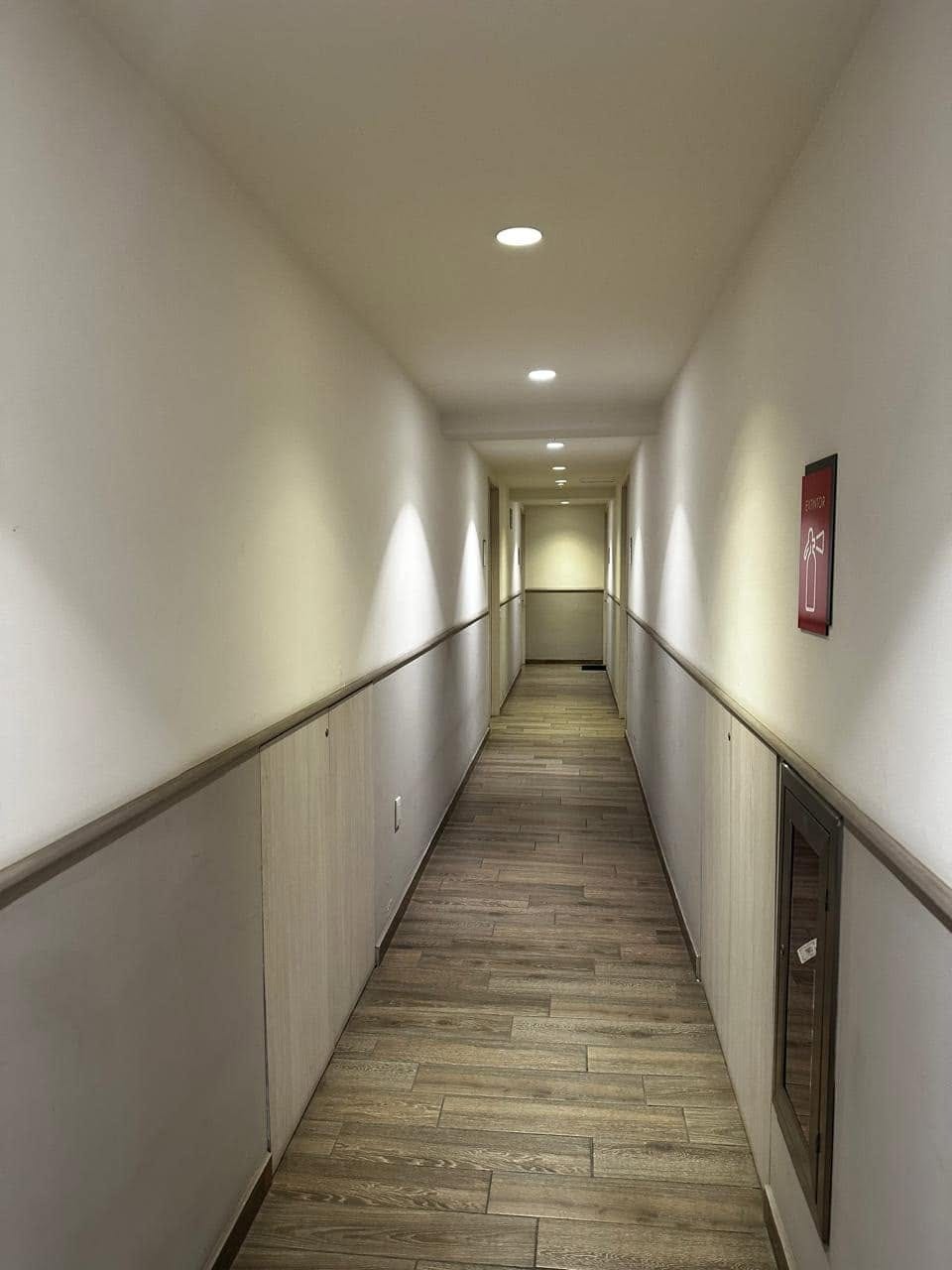 Pasillo interior de acceso a los departamentos, con piso de madera y luz indirecta